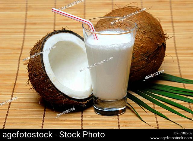 Glass of coconut milk, halved coconut, drinking straw, coconut milk