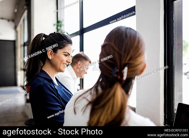 Happy young businesswoman with colleagues standing by window