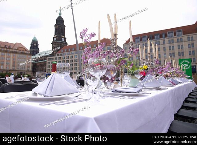 24 April 2020, Saxony, Dresden: An empty covered table stands on the Altmarkt in front of the Kreuzkirche. With orphaned chairs in front of a historical...