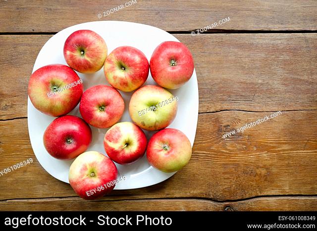 many red apples on white plate over vintage wooden table
