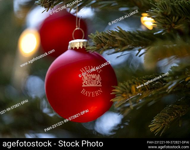 21 December 2023, Bavaria, Munich: Red Christmas baubles with the inscription ""Heimat Bayern"" and the Bavarian coat of arms hang on a Christmas tree in the...