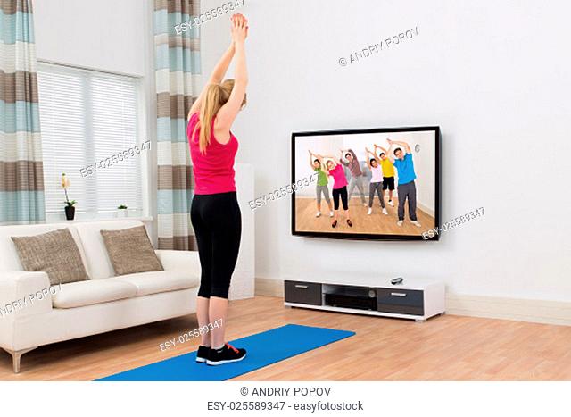 Young Woman Watching Television And Exercising In Living Room At Home