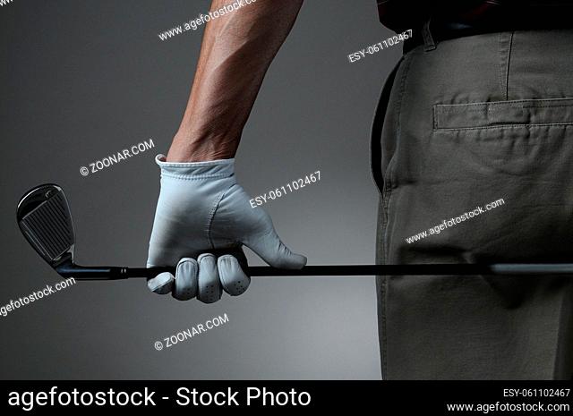 Closeup of a male golfer holding a six iron behind his body. Man has a Golf Glove on his hand. Horizontal format over a light to dark gray background