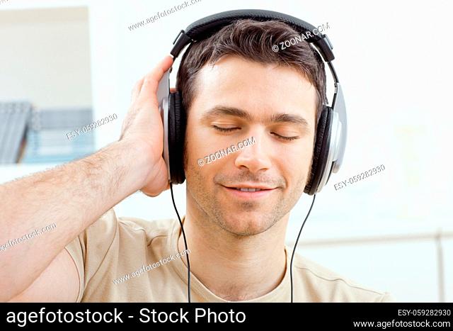 Casual man listening music with headphones at home, relaxing with closed eyes, smiling