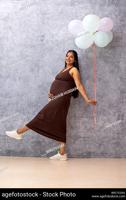 Pregnant woman standing against wall with a bunch of balloons