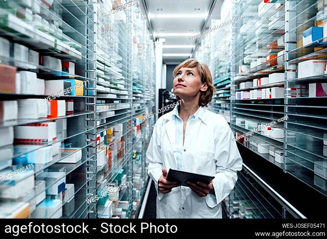 Female pharmacist looking at medicine while holding digital tablet at pharmacy store
