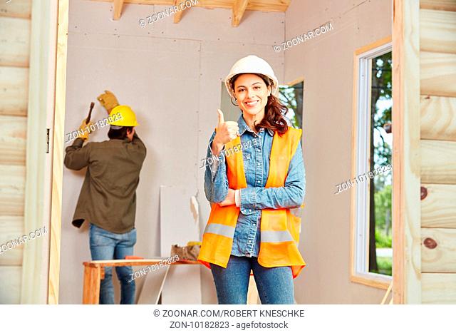 Junge Frau als Handwerker Lehrling hält den Daumen hoch auf Baustelle