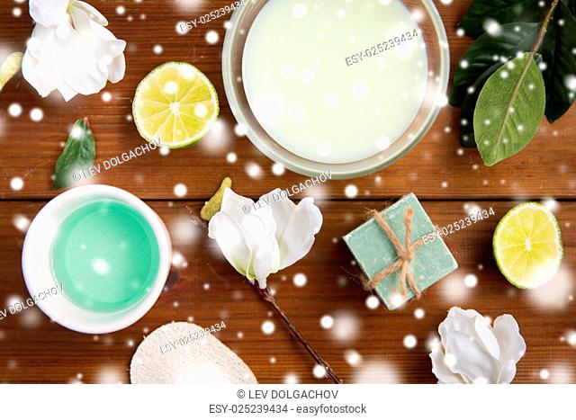 beauty, spa, body care and natural cosmetics concept - bowls with citrus body lotion, cream and handmade soap bar on wooden table over snow