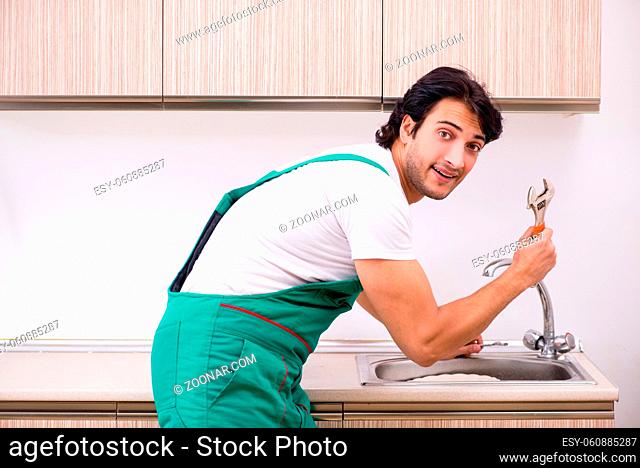 Young plumber repairing tap at kitchen
