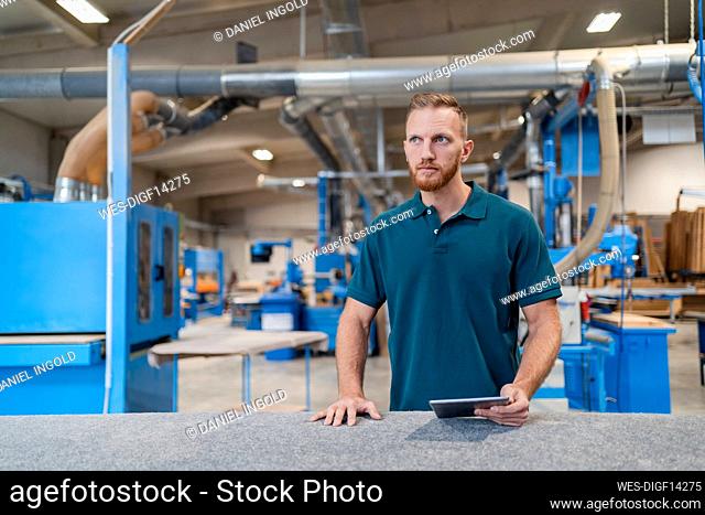 Portrait of carpenter standing in production hall with digital tablet in hand