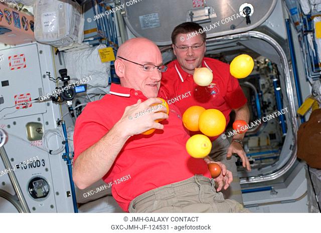 NASA astronauts Doug Wheelock (background), Expedition 25 commander; and Scott Kelly, flight engineer, are pictured near fresh fruit floating freely in the...