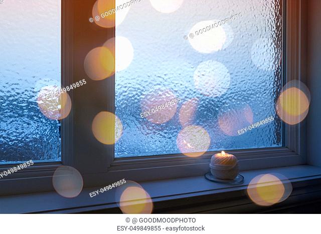 Frosted winter window, burning candle and golden bokeh lights