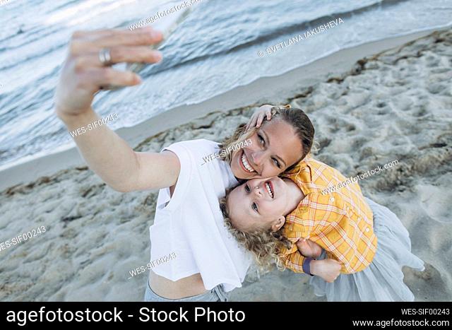 Happy mother with daughter taking selfie through smart phone at beach