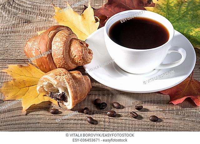 Coffee with a croissant on a wooden table. Grains of coffee and maple leaves on the table