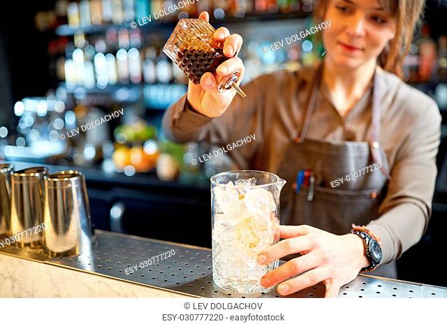 alcohol drinks, people and luxury concept - woman bartender with glass of ice and syrup preparing cocktail at bar