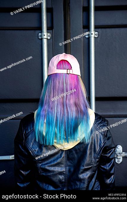Rear view of young woman with dyed hair in front of black container