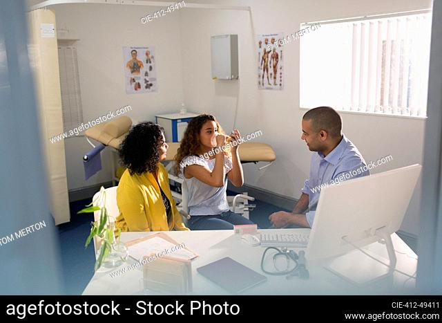 Male doctor teaching girl how to use inhaler in doctors office