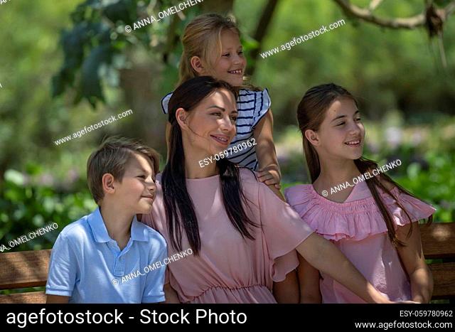 Portrait of a Happy Big Family Outdoors. Looking a Side. Beautiful Young Mother Spending Time with Her Three Precious Kids on Enjoying Fresh Air