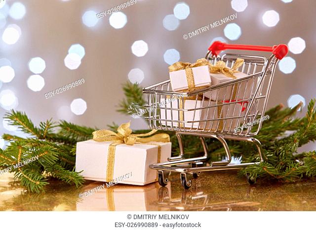 Shopping trolley with gift boxes and brenches of fir-tree with decoration on a grey background with light of garland. Christmas and New Year sale