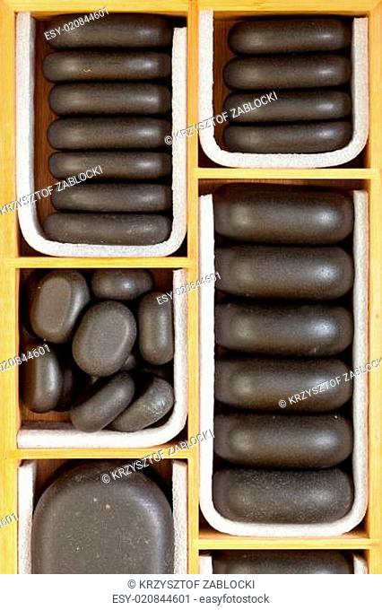 Black spa zen massage stones in wooden case as background