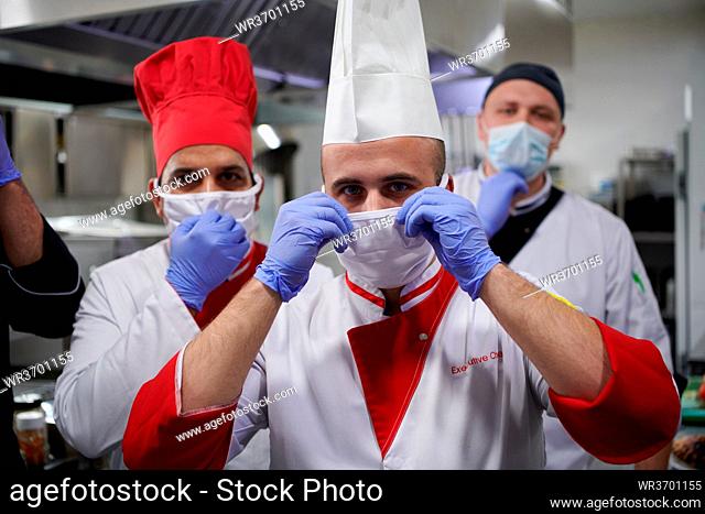 Mixed race team Portrait of group chefs standing together in the kitchen at restaurant wearing protective medical mask and gloves in coronavirus new normal...