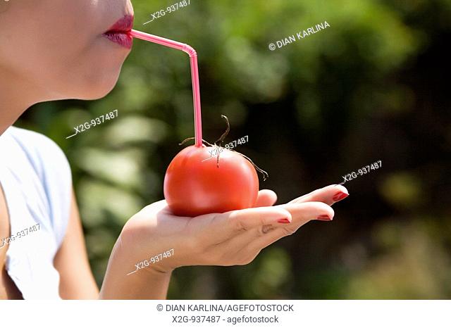 An Asian woman drinking tomato with a plastic straw