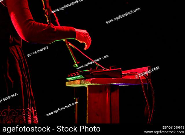 A closeup side profile shot of a musician performing on stage in selective focus by night, hands using electronic mixing equipment against black background