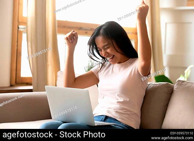Happy millennial vietnamese lady looking at laptop screen, making yes gesture celebrating online lottery win or reading email with last mortgage banking payment...
