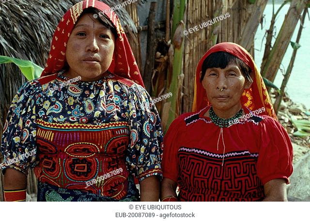 Head and shoulders portrait of Kuna mother and daughter wearing brightly coloured blouses or dulemola with layered applique mola panels and red and yellow head...