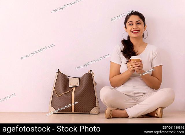 Portrait of happy young woman sitting on floor with holding cold coffee in her hand
