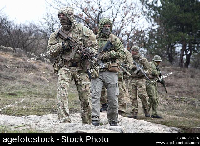 Military team, private military company mercenaries group in camouflage military uniform and mask, armed service rifles, walking in line behind commander