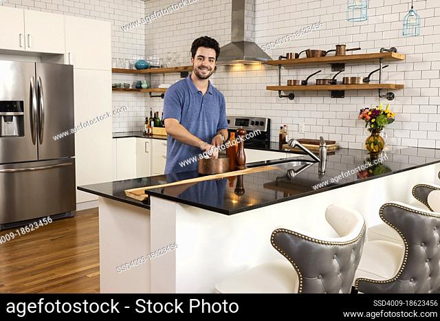 Portrait of a young man in a modern kitchen looking at camera and cooking a meal