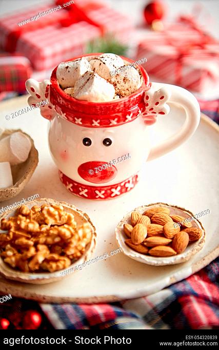 Delicious homemade christmas hot chocolate or cocoa with marshmellows in a red xmas decorative cup. With almonds, walnuts in small bowls on side