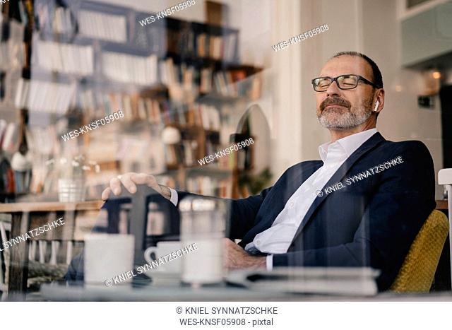 Mature businessman listening to music with bluetooth earbuds in a cafe