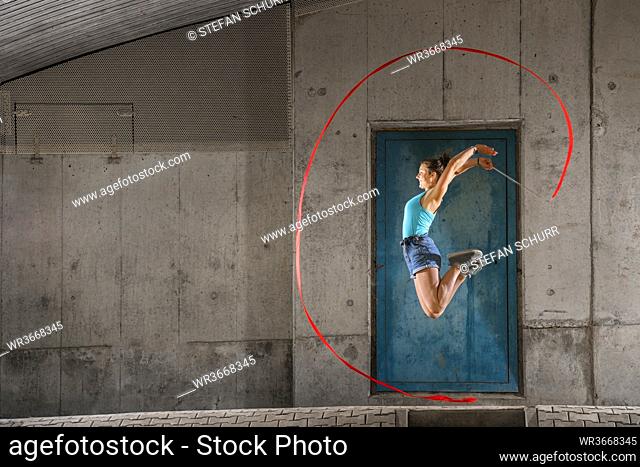 Young woman holding ribbon jumping while doing aerobics against concrete wall