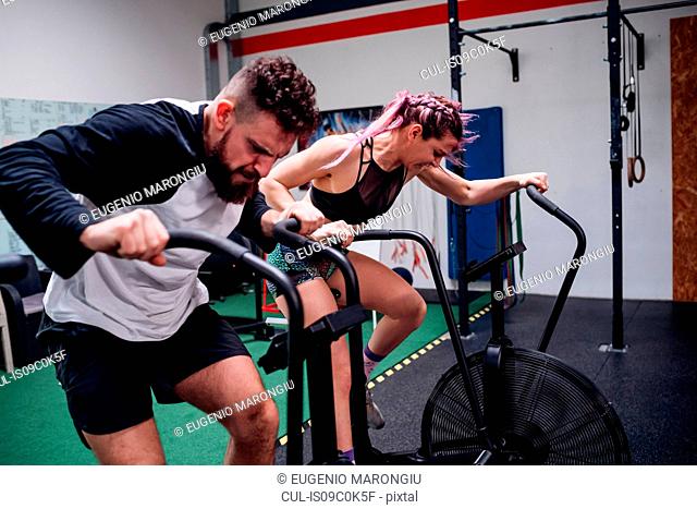 Young woman and man training together on gym exercise bikes, action