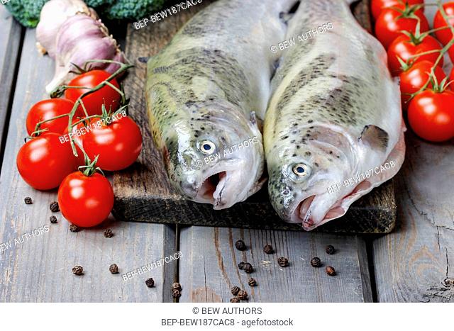 Two rainbow trouts, tomatoes and garlic on rustic wooden table