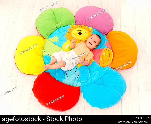 Happy baby lying on colorful flower playmat, smiling, elevated view