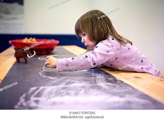 3-6 years old girl drawing with chalk on a table board