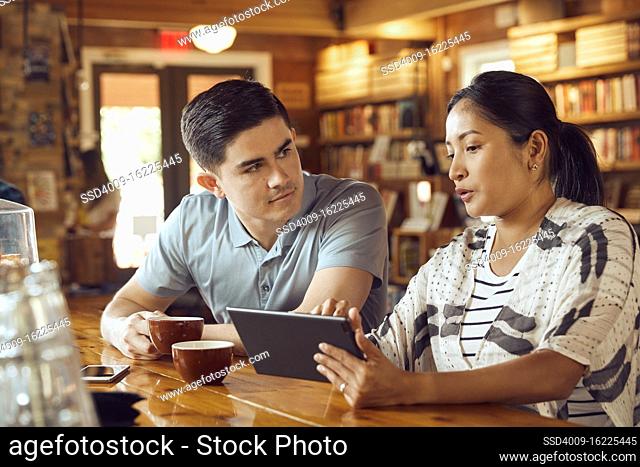 Young man and woman sitting at counter in cafe bookstore looking at tablet