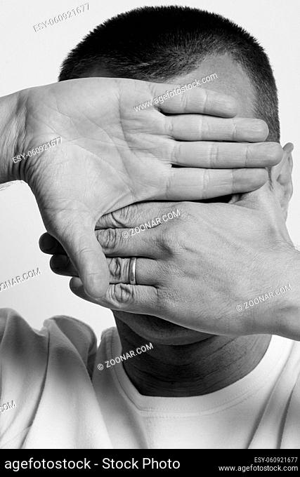 Man in white t-shirt covering his face with hands over gray background. High quality photo