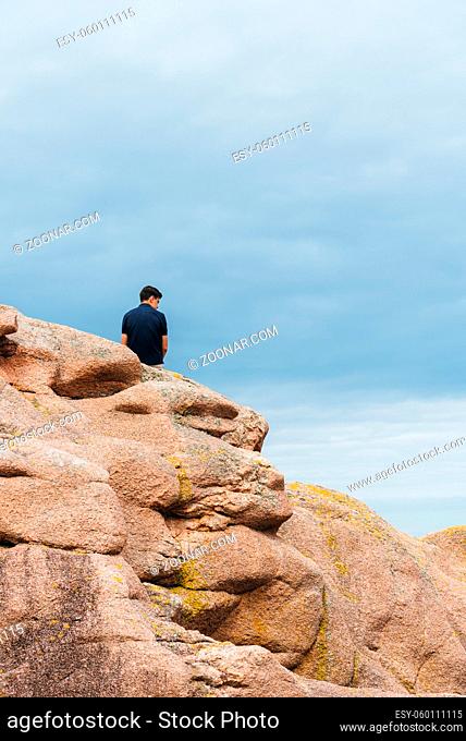 Young man on top of rock formations in Pink Granite Coast around Perros-Guirec in Brittany, France