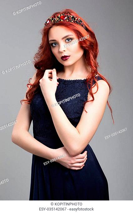 Beautiful red-haired fashion model posing in evening dress over dark background
