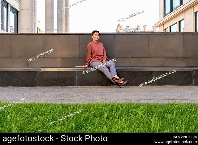 Businesswoman sitting on bench by footpath at city