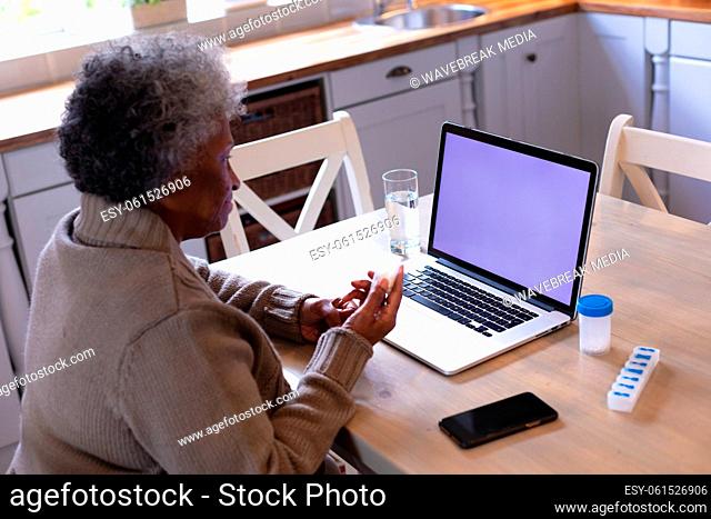 African american senior woman holding empty medication container while having a videocall on laptop