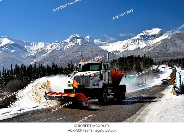 A truck plowing snow along the side of the road on a bright winters day in the rocky mountains of Alberta Canada