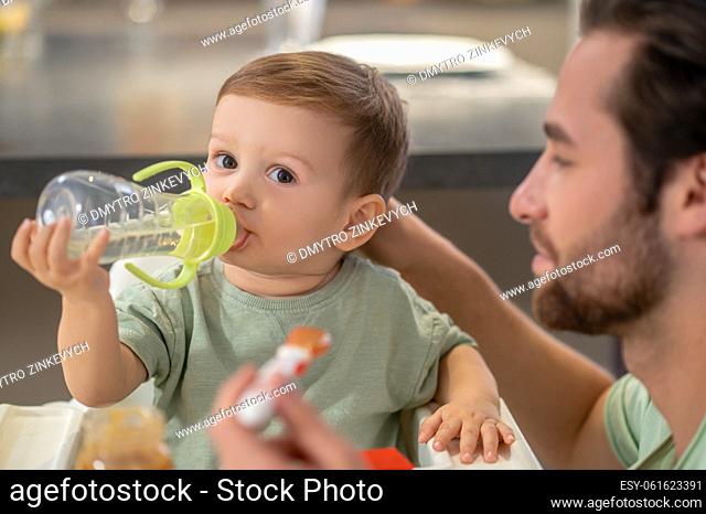 Eating. Cute little boy drinking from his bottle while dad feeding him