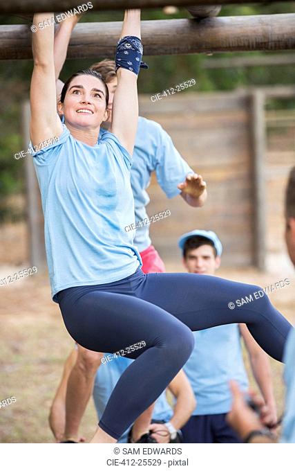 Smiling woman crossing monkey bars at boot camp