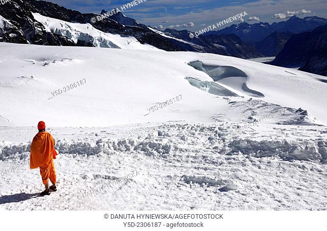 Asian Ethnicity barefoot (actually only in sandals) monk in traditional robe admiring view from the top of Jungfraujoch in Swiss Alps, Switzerland