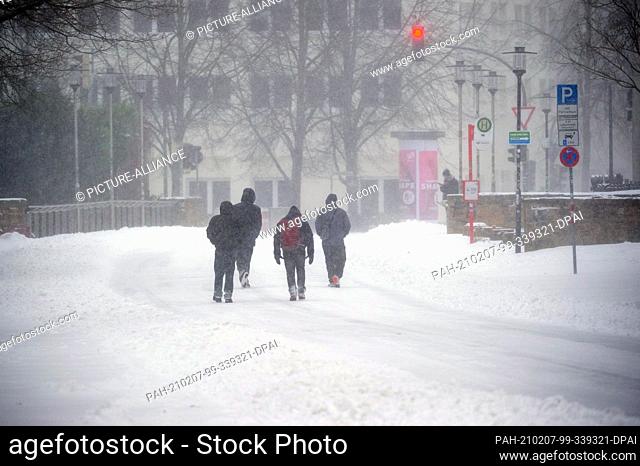 07 February 2021, Lower Saxony, Osnabrück: Four people are walking in dense snow drifts on the partially cleared roadway
